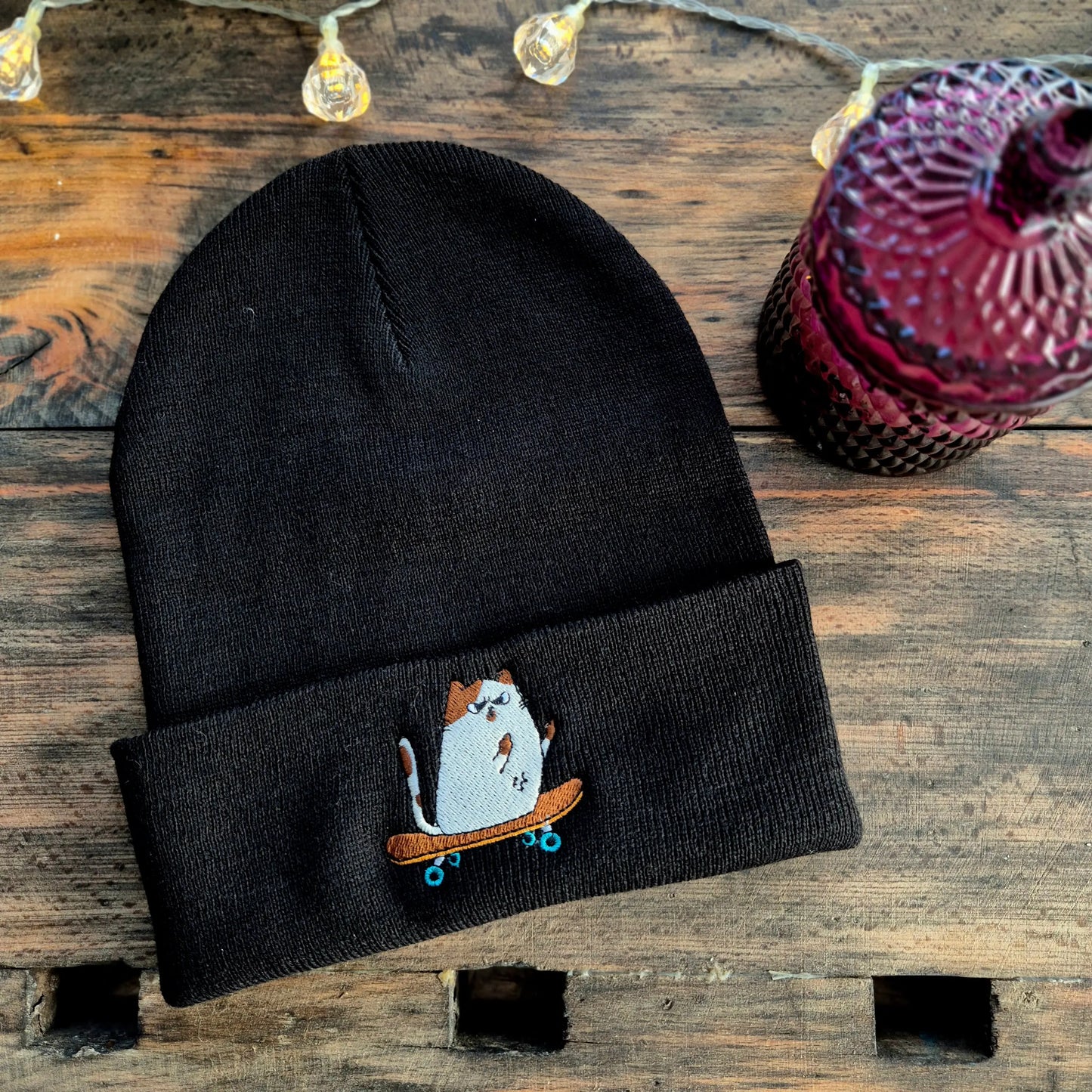 gestickte Katze auf dem Skateboard zeigt Mittelfinger auf einer Beanie