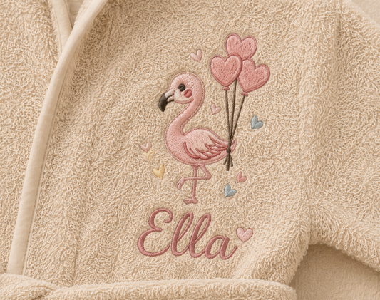 Detailansicht der personalisierten Flamingo-Stickerei mit Namen Ella auf einem beigen Baby-Bademantel. Hochwertige individuelle Bestickung auf weichem Frottee mit Herzballon-Motiv.